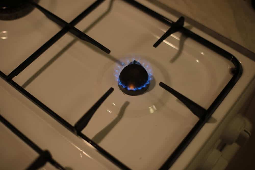 A lit gas burner on a white stovetop with visible blue flames, perfect for home salvage projects after fire damage.
