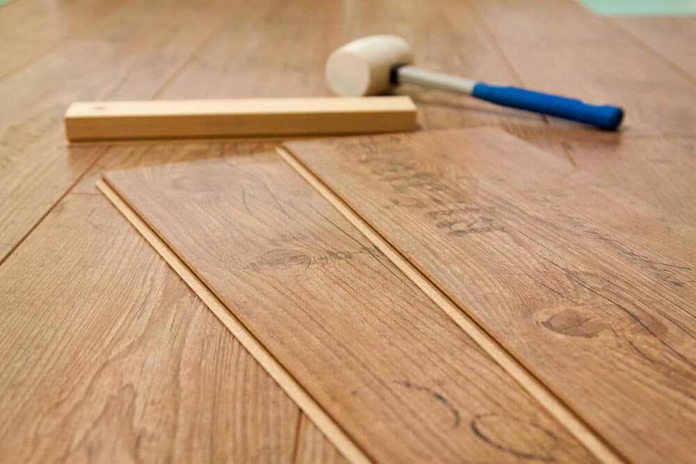 Close-up of laminate flooring planks being installed with a rubber mallet and wooden block lying on the floor. This simple guide shows the tools needed to fix laminate floors, ensuring a seamless installation process.