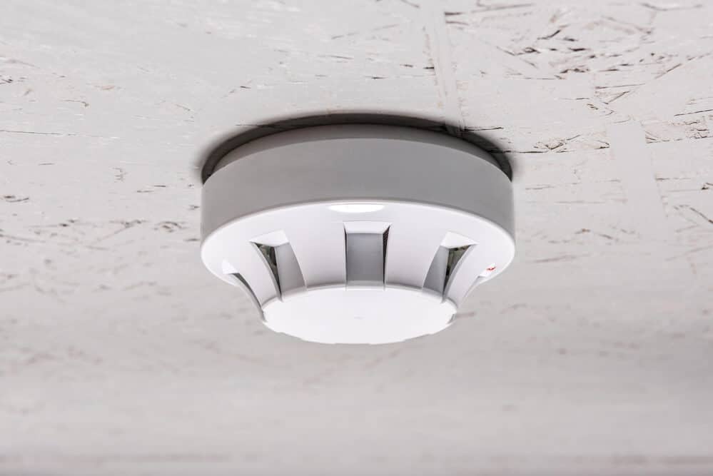 A white smoke detector is mounted on a textured ceiling, an essential device when learning how to get fire smoke smell out of the house effectively.