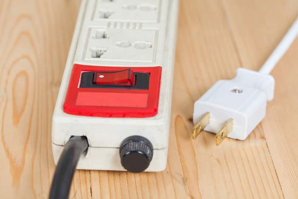 A power strip with a red on/off switch lies on a wooden surface, next to a white power plug—a crucial tool for both businesses and homes to manage their electronics efficiently.