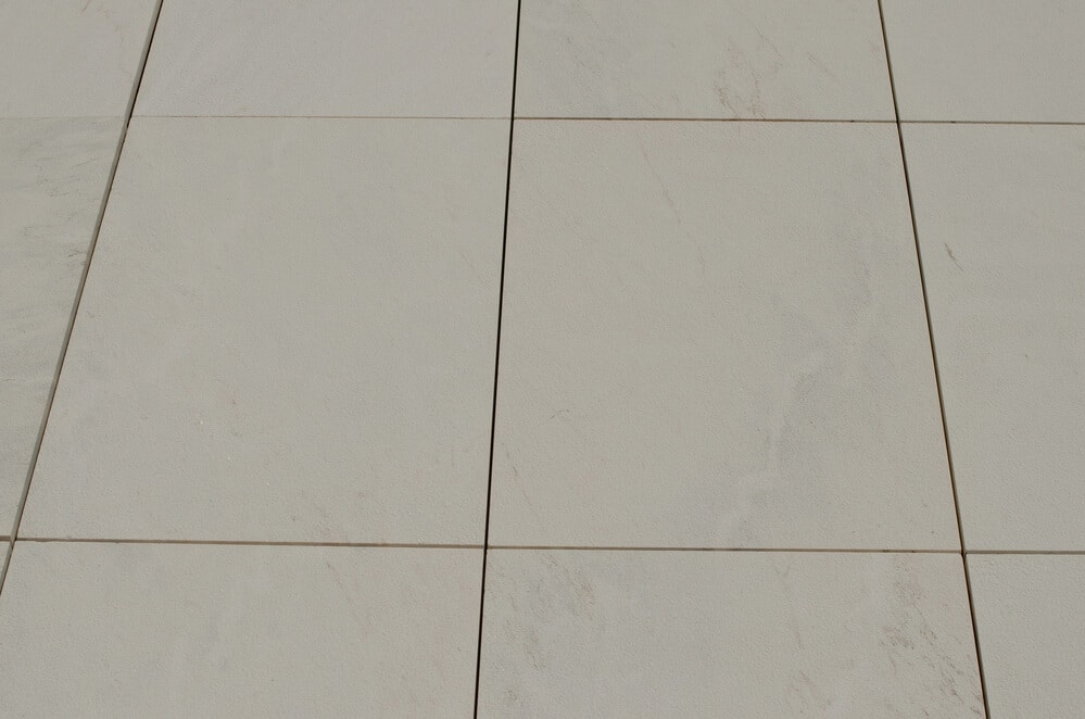 A close-up view of a light-colored tiled floor with subtle vein patterns and meticulously clean grout lines intersecting at right angles.