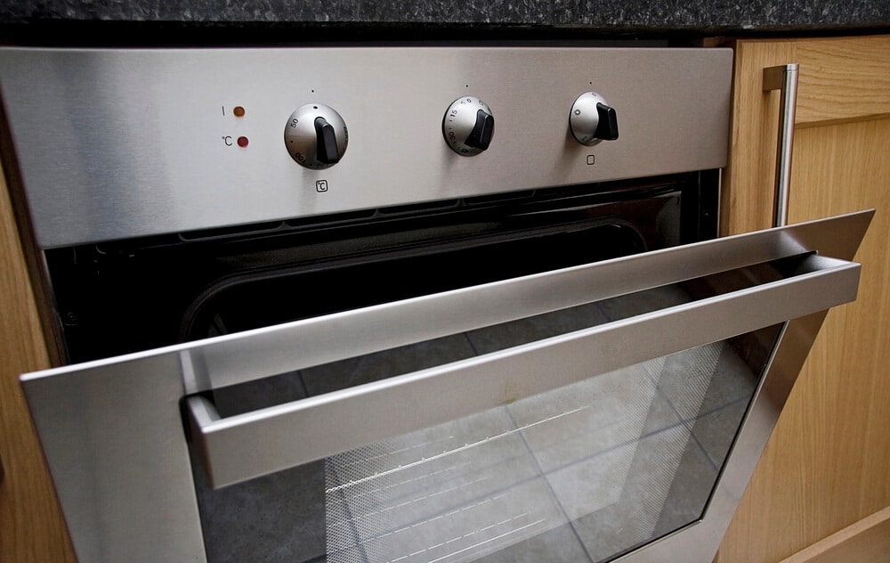 A stainless steel oven with the door partially open, revealing the interior. The oven has three control knobs on the front panel and features essential kitchen safety elements to help put out fires quickly and efficiently.