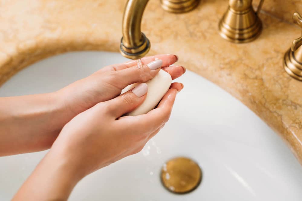 A person washing their hands with a bar of soap under a brass faucet, ensuring cleanliness and hygiene.